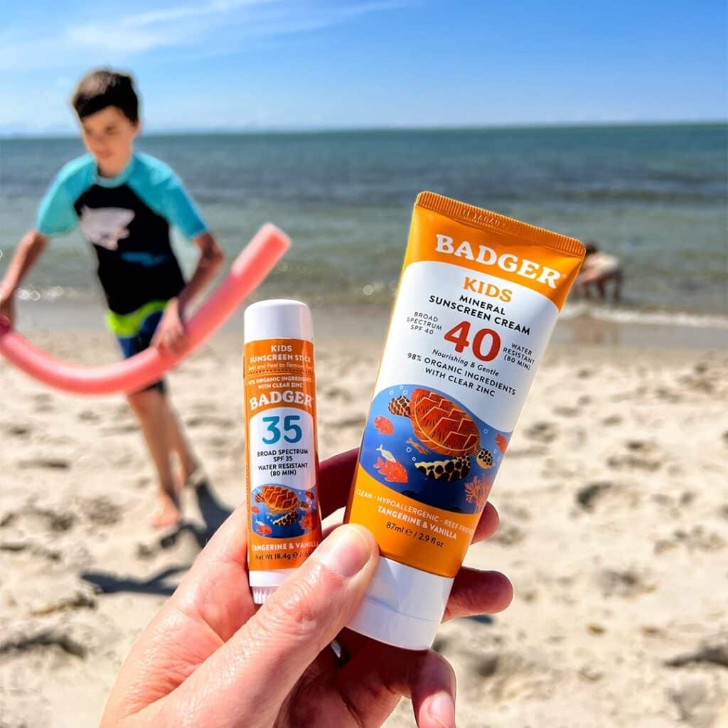 Badger is one of the best non toxic mineral sunscreen for kids. Here i'ts hold n the front wwith a kid running in the background at a beach