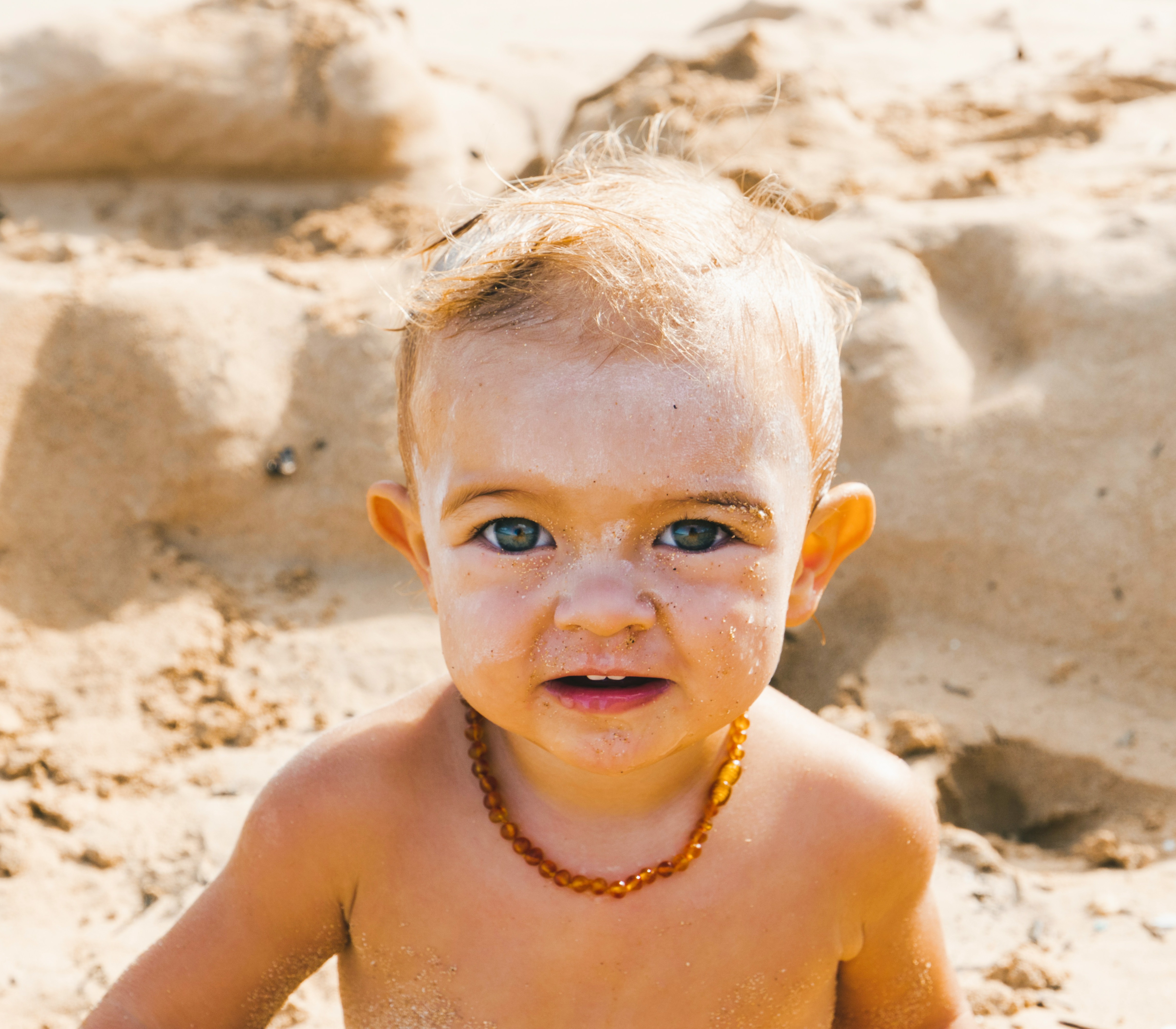 baby sitting at the beach with sunscreen on his face