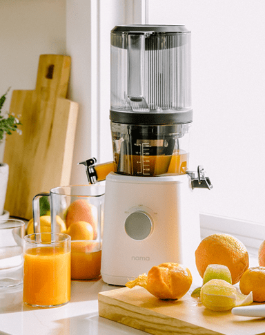 A nama juicer on a countertop with orange and a freshly made orange juice