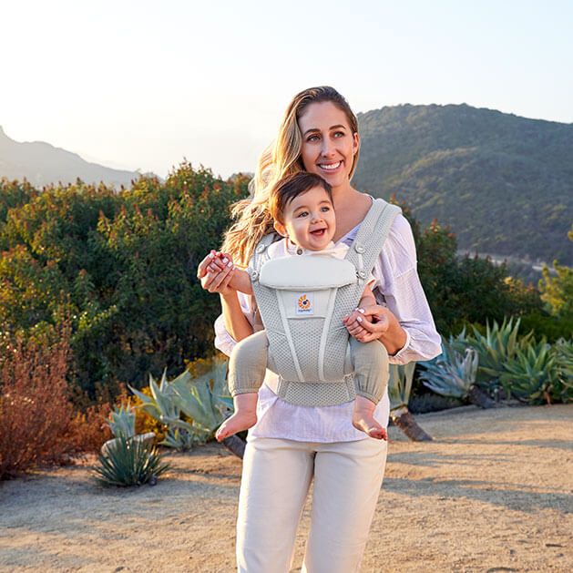 A mom holding her baby in a ergo baby carrier, one of the must-haves when traveling with kids