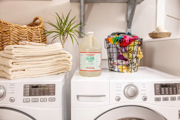 a bottle of dr bronners laundry on top of a washing machine. surrounded by a pile of towel and a basket full of clothes. Non-toxic laundry detergents
