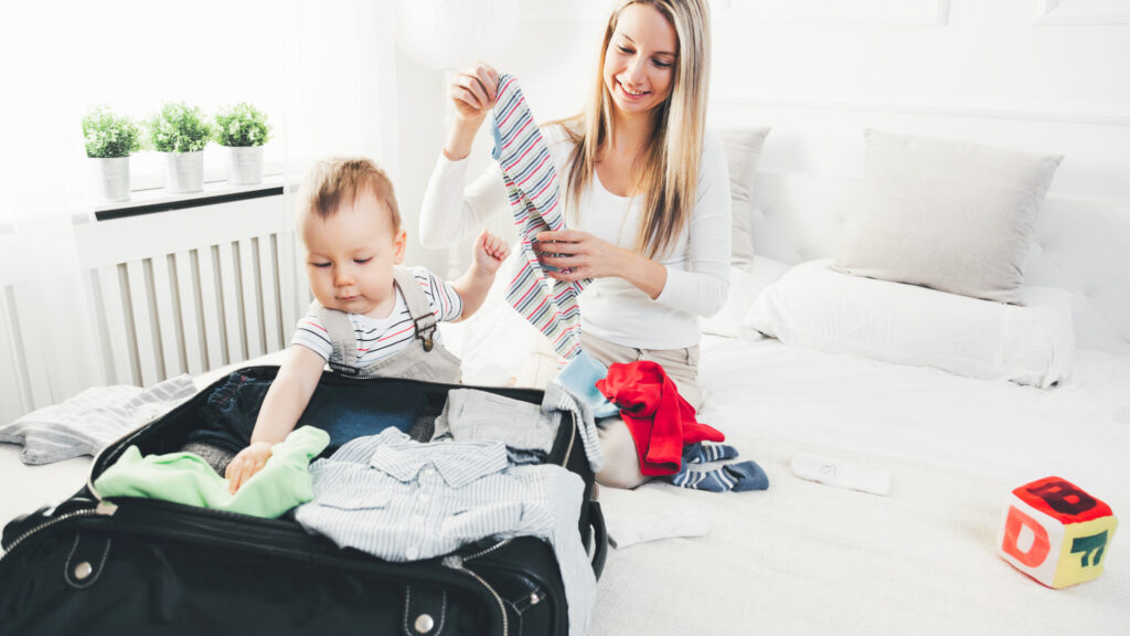 A baby helping his mom pack a suitcase. Suitcase full of clothes 