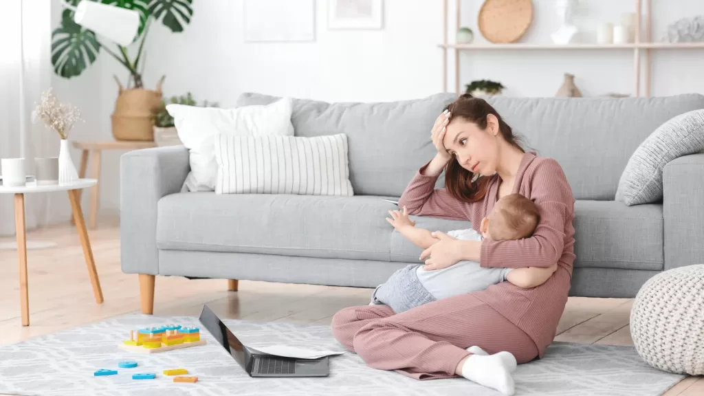 a mom sittin gon the floor breastfedding her baby in front of a laptop. Sleep hacks for moms