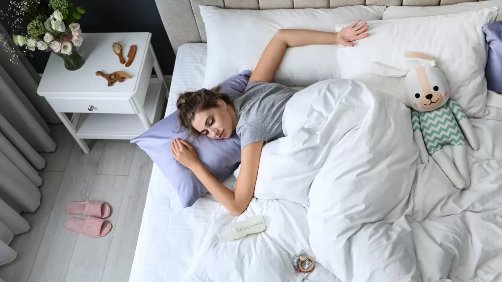 A mom laying down in a bed slpeein ghacks for mom to help them sleep better