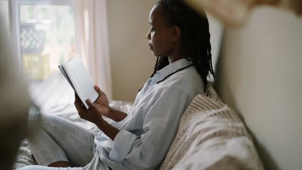 a mom sitting in bed, reading a book in her pyjama befor going to sleep