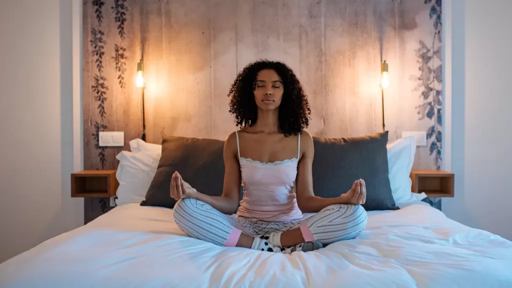 relaxation activities like yoga before goinf to bed is one of the best sleep hack for moms. A woman sitting on her meditating with dimmed lights