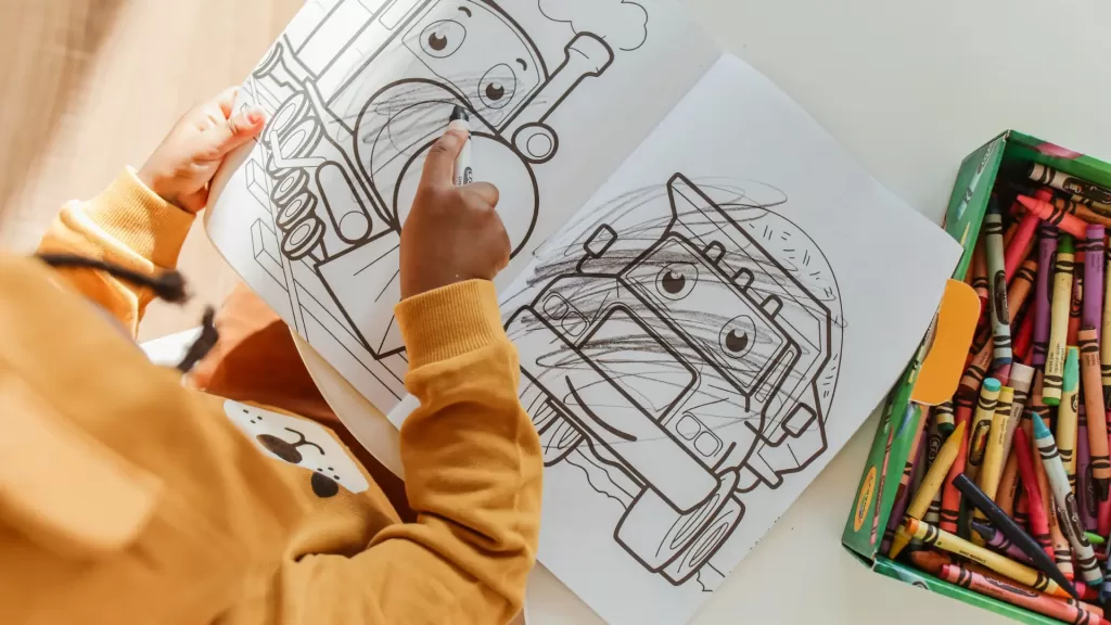 When traveling with toddlers it's essential to pack coloring books and activities. Image of a coloring page with a baby hand drawing all over the page